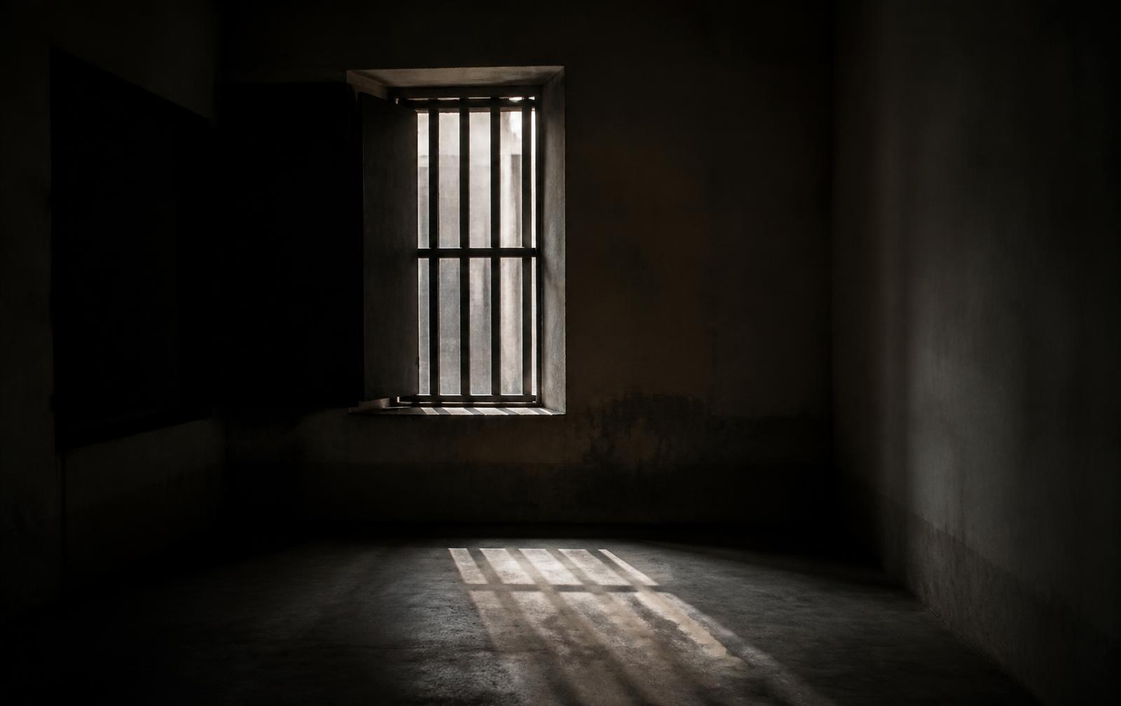 A dark, quiet room with soft daylight entering through a partially obstructed window, casting long shadows